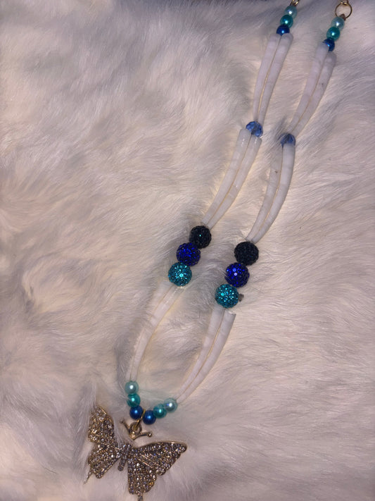 Dentalium Necklace with blue and black beads and a butterfly charm on a white fur background